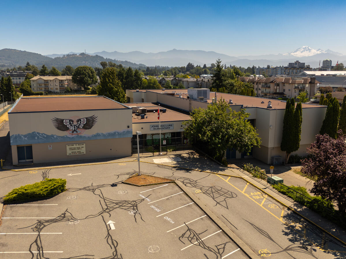 Exterior image of the entrance to an elementary school. Background has mountain range, trees and city structures.