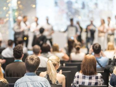 Photo taken of a stage behind the audience, audience is in focus. Performers on the stage are out of focus.