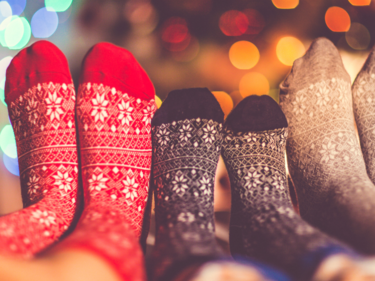 A photo of three people's Christmas themed socks with a Christmas tree out of focus behind them.