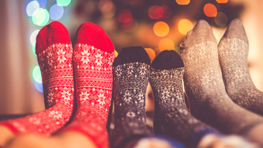 A photo of three people's Christmas themed socks with a Christmas tree out of focus behind them.