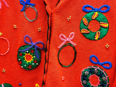 A close up photo of a red Christmas sweater covered in beaded wreaths with bows.