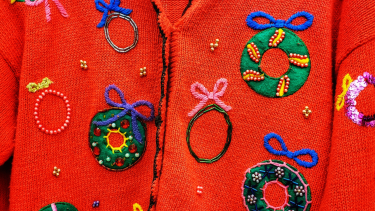 A close up photo of a red Christmas sweater covered in beaded wreaths with bows.