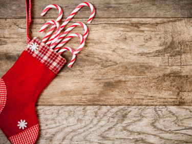 Photo of a red Christmas stocking full of candy canes against a wooden backdrop.
