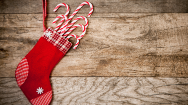 Photo of a red Christmas stocking full of candy canes against a wooden backdrop.