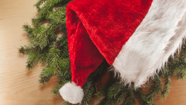 Photo of a Santa hat laid out onto some garland on a table.