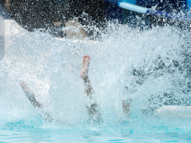 Photo of a child coming down a waterslide and splashing into the pool.
