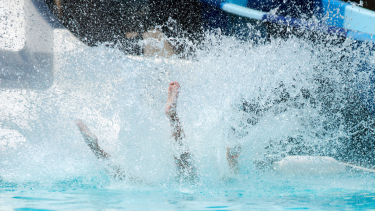 Photo of a child coming down a waterslide and splashing into the pool.