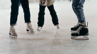 A photo of three people wearing skates standing on ice. Photo is from the knees down.