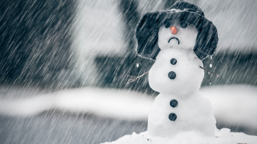 Photo of a snowman wearing a hat with a sad face in the rain.