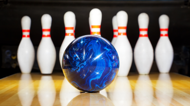 Image of a blue bowling ball in front of bowling pins set up in a lane.
