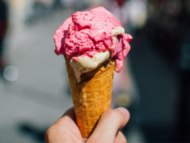 A photo of a strawberry ice cream cone being held.