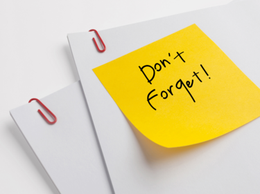 Photo of some paper that has been paperclipped together. A yellow sticky note on the package says "Don't forget!"