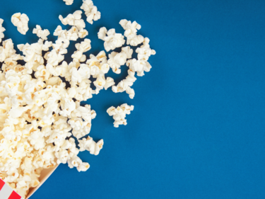 Photo of popcorn spilled over a blue background.