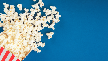 Photo of popcorn spilled over a blue background.