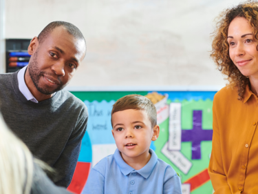 A photo of a young boy and his parents meeting his teacher in their classroom.