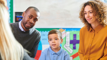 A photo of a young boy and his parents meeting his teacher in their classroom.