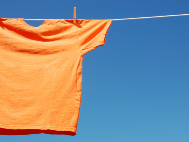 An orange shirt hanging from a clothes line in front of a blue sky.