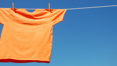 An orange shirt hanging from a clothes line in front of a blue sky.