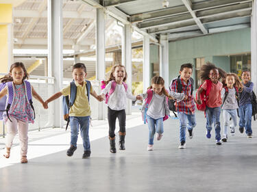 Photo of 8 elementary aged kids running down a hallway holding hands.