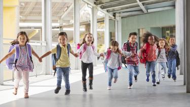 Photo of 8 elementary aged kids running down a hallway holding hands.