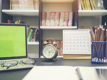 Photo of a desk with laptop, clock, and calendar.