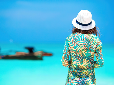 Photo of a women standing in front of the ocean wearing a sunhat and floral shirt