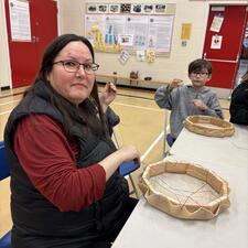 A parent volunteer works on her drum next to her child